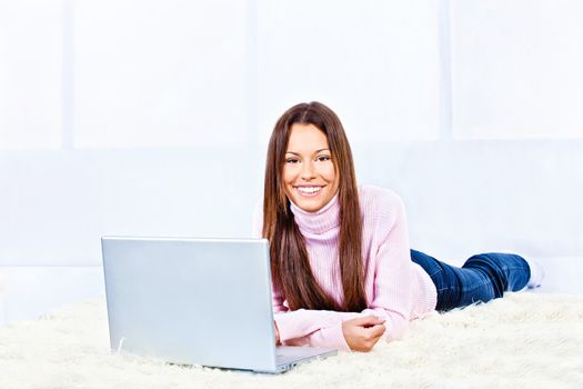 Pretty young woman with laptop on carpet at home