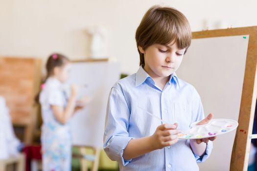 Image of little cute boy painting pictures at kindergarten