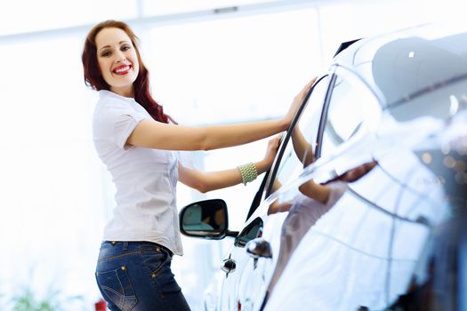 Pretty woman standing near car at car center. Choosing a car