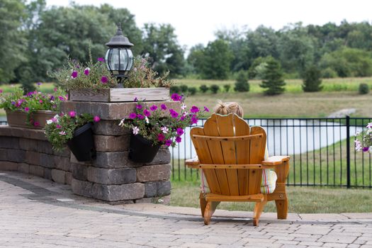 Person relaxing in a garden chair with their back to the camera overlooking open countryside and a small lake