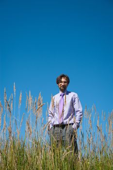 man in a tie standing in a field on a background of blue sky