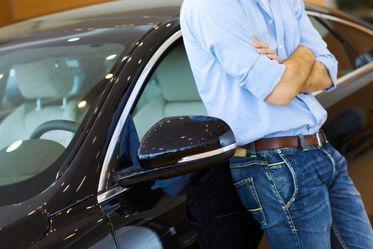 Handsome young man consultant at car salon standing near car