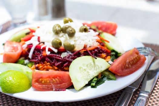 Closeup view of a plate of fresh mixed salads and vegetables with tomato, cucumber and lemon in the foreground