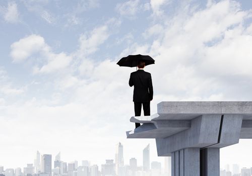 Image of businessman with umbrella standing at the edge of bridge