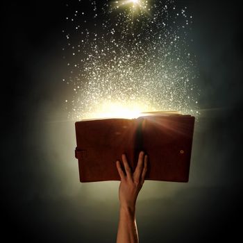 Human hand holding magic book with magic lights