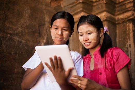 Portrait of two beautiful young traditional Myanmar girl using digital tablet pc together.