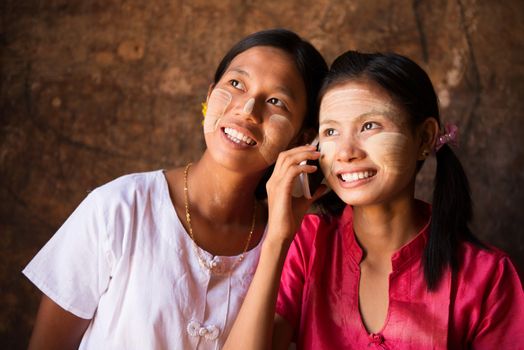 Portrait of two beautiful young traditional Myanmar girls using smart phone.