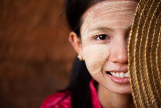 Portrait of beautiful shy young traditional Myanmar girl with straw hat smiling. Close up head shot.
