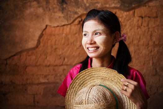 Portrait of beautiful young traditional Myanmar girl with straw hat looking away. 