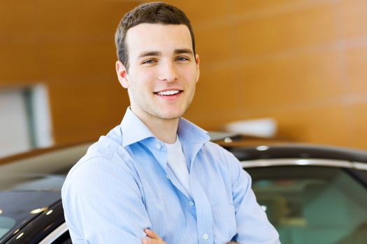 Handsome young man consultant at car salon standing near car