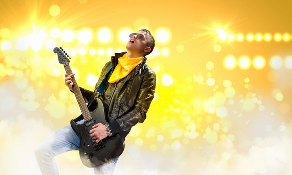 Young man, rock musician in jacket playing guitar