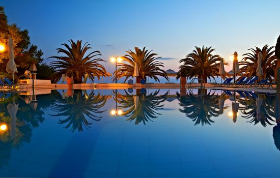 Swimming pool with palm trees by the evening sea