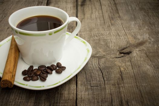A coffecup with coffee beans and a cinnamon stick on wooden background