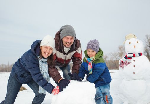Happy beautiful family building snowman outside in winter time