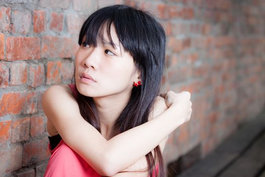 Young Asian woman sitting by red brick wall feeling depressed and sad