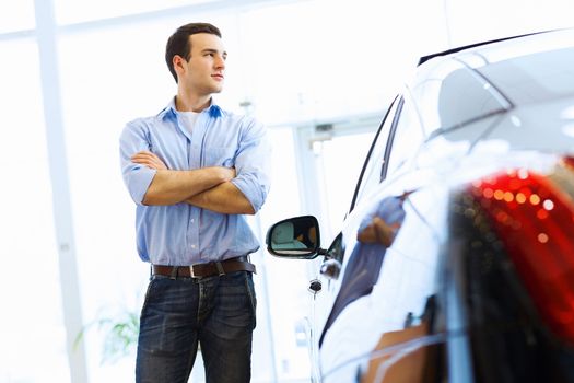 Handsome young man consultant at car salon standing near car