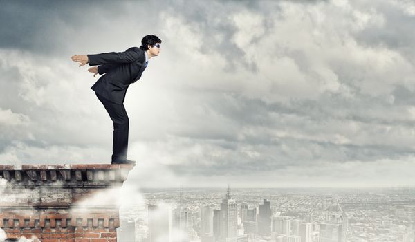 Image of young businessman in goggles jumping from top of building