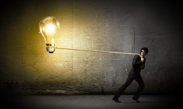 Image of young businessman pulling bulb with rope