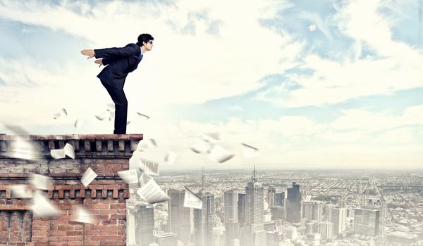 Image of young businessman in goggles jumping from top of building