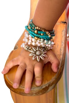 Closeup of a little girls hand and wrist resting on the arm of a wooden chair adorned with colourful beads and bracelets