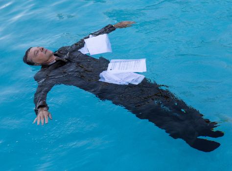 Senior caucasian businessman in suit sinking underwater in deep blue pool worried about being underwater with mortgage payments