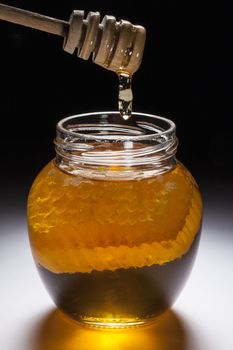 A jar of farmhouse honey with part of a honeycomb in the jar. Honey is a sweet food made by bees using nectar from flowers. The variety produced by honey bees  is collected by beekeepers and consumed by humans.