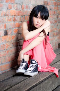 Young Asian woman sitting by red brick wall feeling depressed and sad