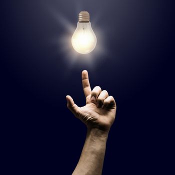 Human hand pointing with finger at electrical bulb