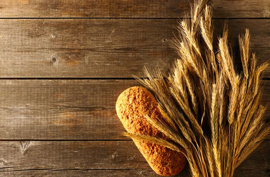 Rye spikelets and bread on wooden background