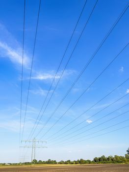 Power cable and power pole in a field under a blue sky with white clouds