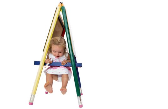 Small barefoot girl having fun swinging on a signboard, hanging on the cross bar with her feet in the air, isolated on white