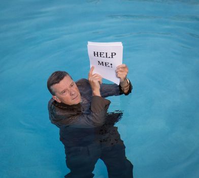 Senior caucasian businessman in suit up to neck in deep blue water worried about drowning in paperwork and holding help me document