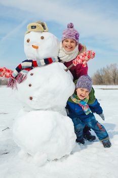 Happy beautiful children with snowman outside in winter time