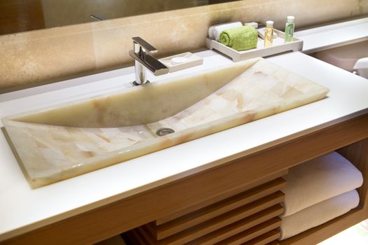 Modern marble handbasin in a hotel bathroom in a wooden vanity unit with toiletries and fresh towels