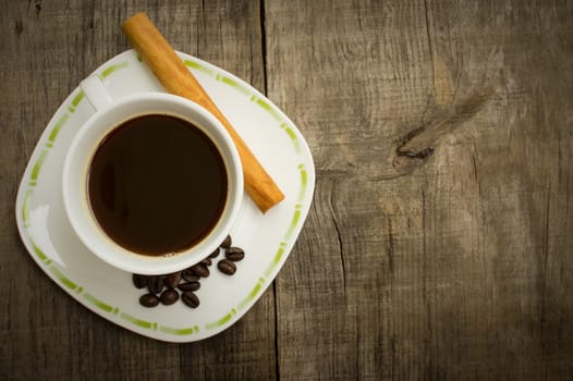 A coffecup with coffee beans and a cinnamon stick on wooden background
