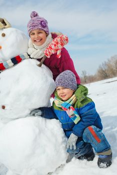 Happy beautiful children with snowman outside in winter time