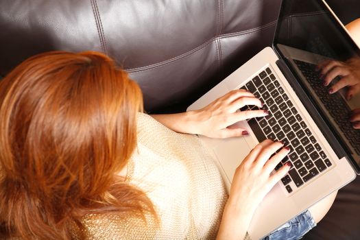 A young adult woman typing on a laptop while relaxing on the sofa.