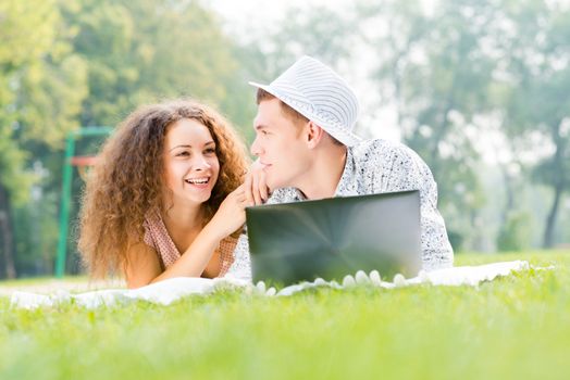 couple lying together in a park, working together on a laptop