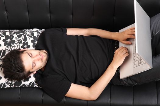 A young hispanic man with a laptop on the Sofa.