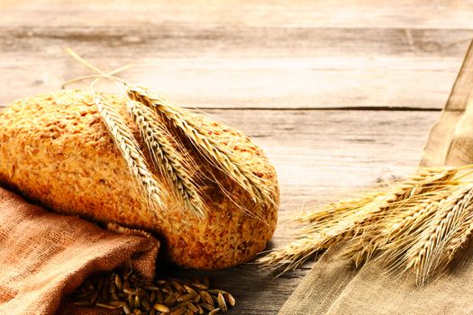 Rye spikelets and bread on wooden background