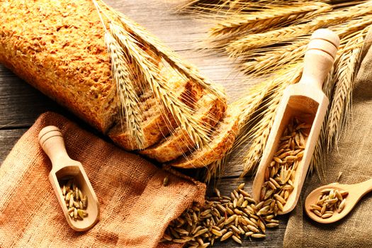 Rye spikelets and bread on wooden background