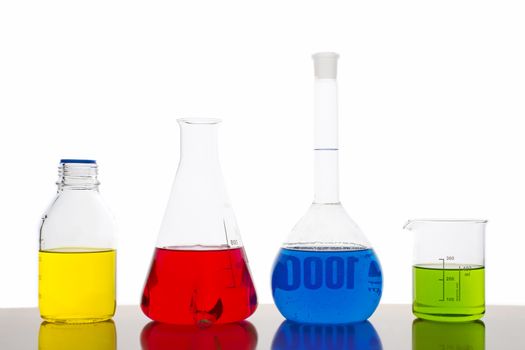 Four measuring glasses on a table of a chemical laboratory with red, yellow, blue and green liquid on white background