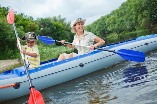 Happy young boy with mother paddling kayak on the river in lovely summer day