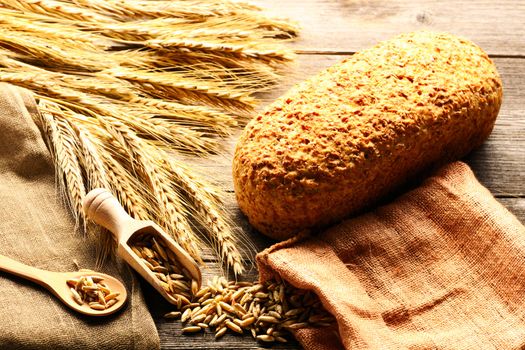 Rye spikelets and bread on wooden background