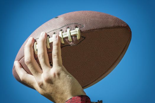 closeup of a hand with american football and blue sky in background