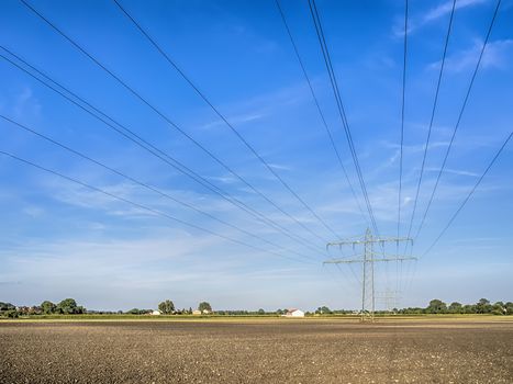 Power cable and power pole over a field under a blue sky with white clouds