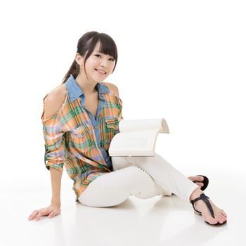 Young asian woman sitting on the ground and reading a book. Portrait isolated on white background.
