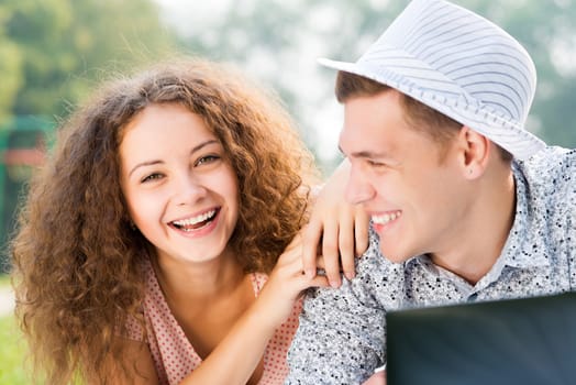 couple lying together in a park, working together on a laptop