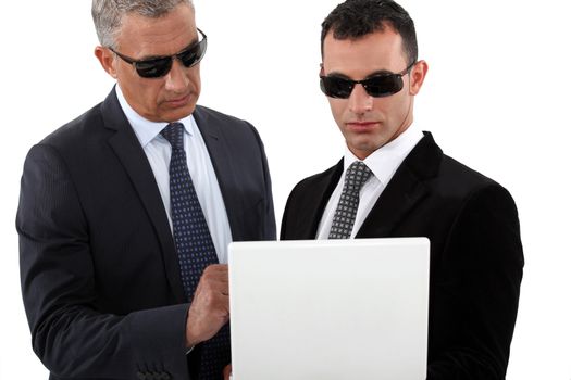 Serious men in smart suits with sunglasses holding a laptop