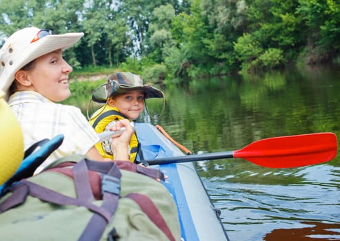 Happy young boy with mother paddling kayak on the river in lovely summer day